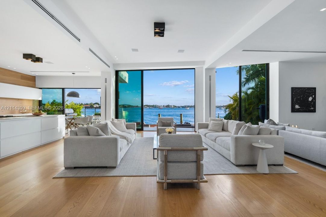 Open-concept living space featuring wood-finish flooring, floor-to-ceiling glass wall systems, flush-mount lighting, and custom cabinetry