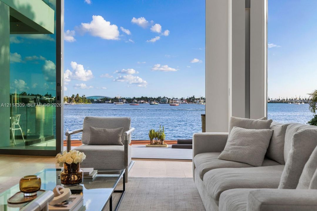 Full-height sliding glass doors opening to a waterfront terrace, featuring neutral large-format tile flooring