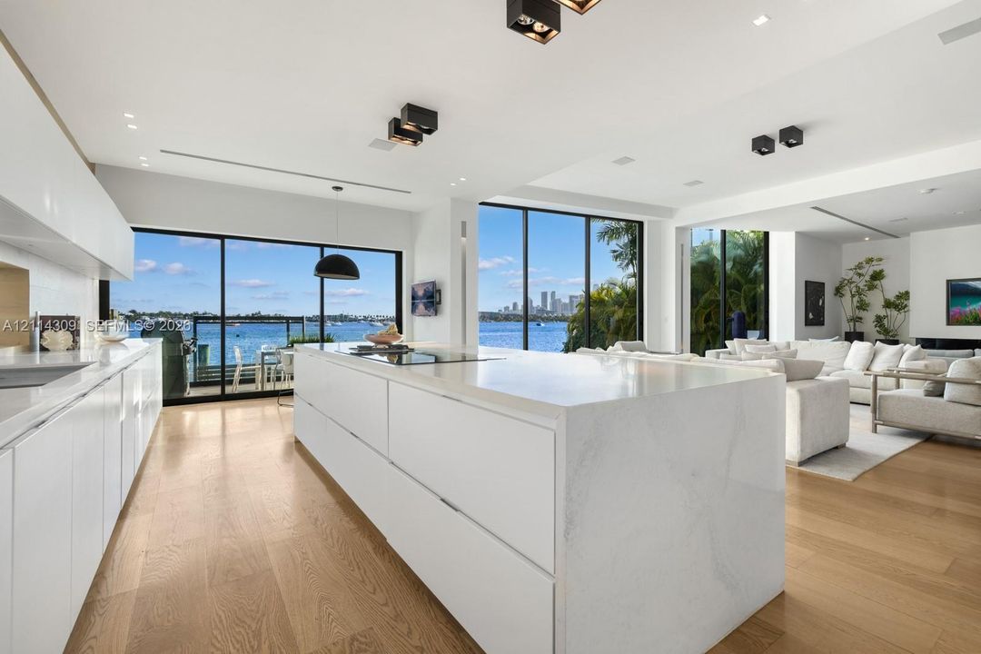 Modern kitchen featuring a waterfall-edge island, flat-panel cabinetry, wood-finish flooring, recessed ceiling lighting, and floor-to-ceiling glass wall panels