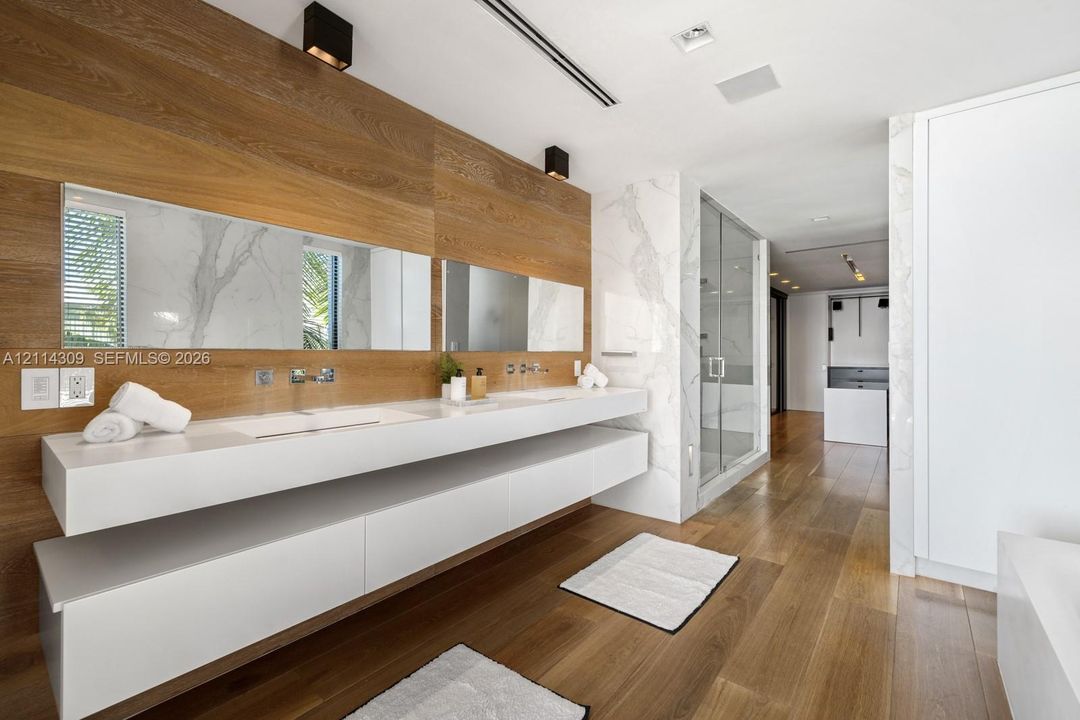 Floating double vanity with integrated sinks, stone wall accents, wood-finish flooring, and glass-enclosed shower