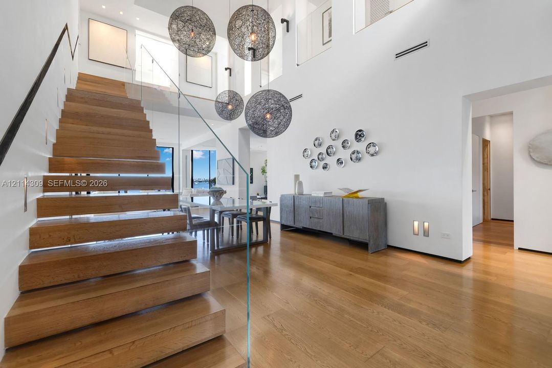 Floating wood-finish staircase featuring a glass panel railing, vaulted ceilings, and multi-tiered spherical pendant lighting
