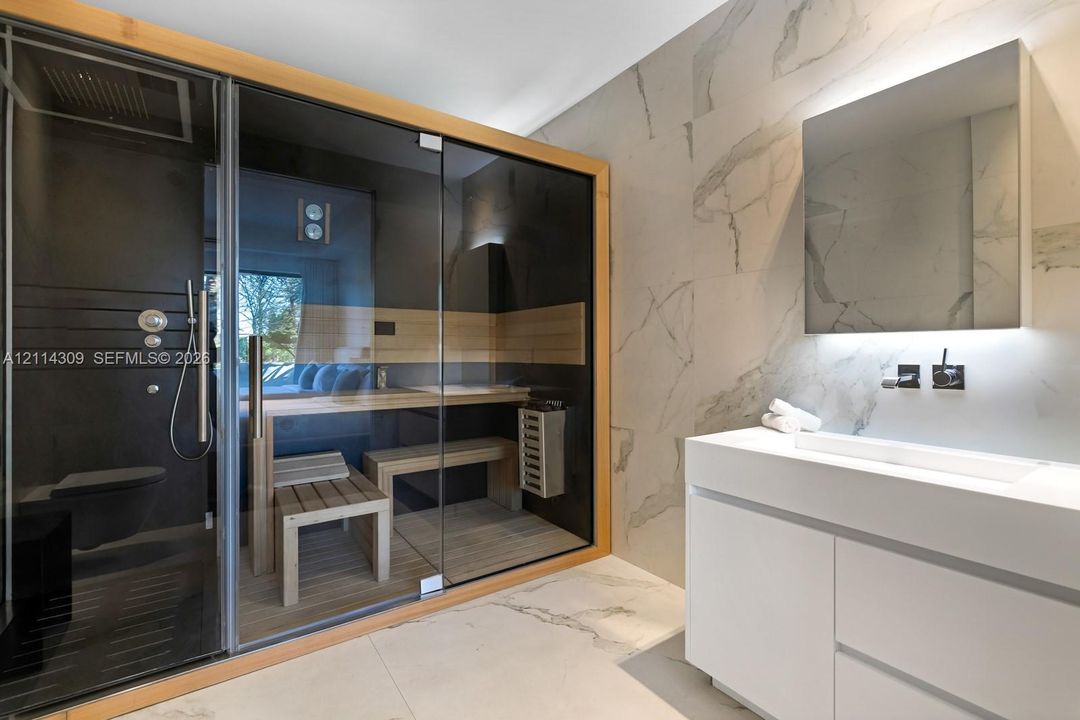 Glass-enclosed sauna with wood bench seating, floating white vanity, stone-finish wall tiles, and wall-mounted faucet fixtures