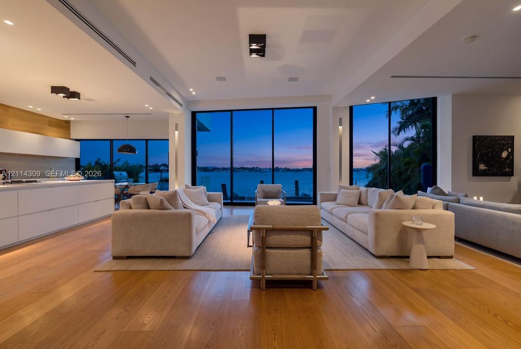 Open-concept interior featuring wood-finish flooring, floor-to-ceiling glass panel walls, integrated recessed lighting, and a minimalist kitchen with flat-panel cabinetry