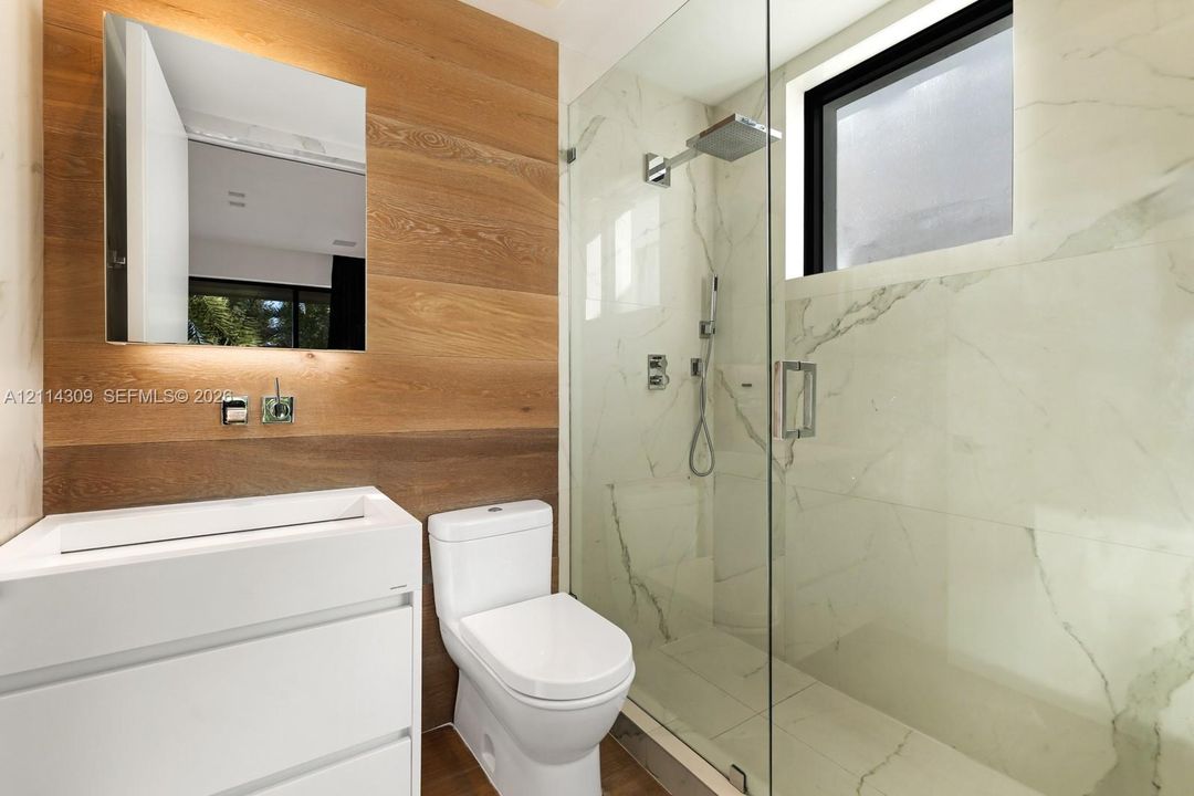 Modern bathroom featuring a wood-finish wall accent, white vanity with integrated basin, walk-in glass shower with stone-finish tiling, and wall-mounted rain shower head