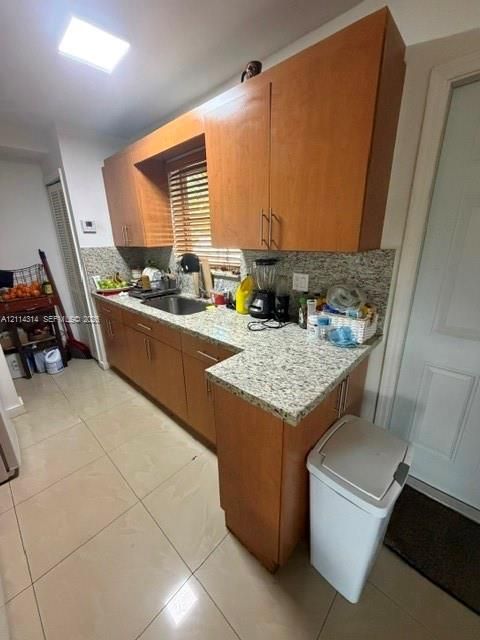 Kitchen featuring light-finish wood cabinetry, stone-texture countertops, tile flooring, and a stainless steel undermount sink