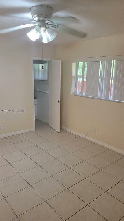 Neutral-toned room featuring large-format tile flooring, a multi-blade ceiling fan with integrated lighting, and a wide window with vertical blinds