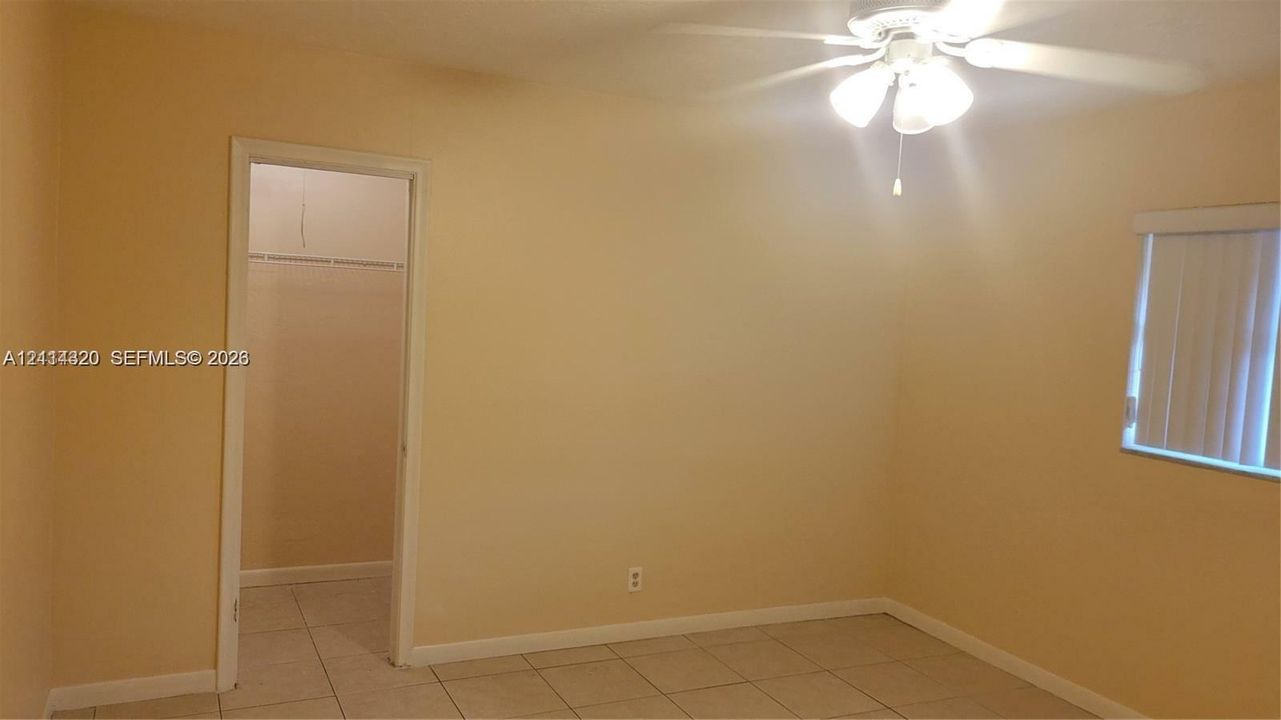 Neutral interior space featuring tile flooring, a multi-blade ceiling fan with integrated lighting, and a closet with a built-in wire shelf
