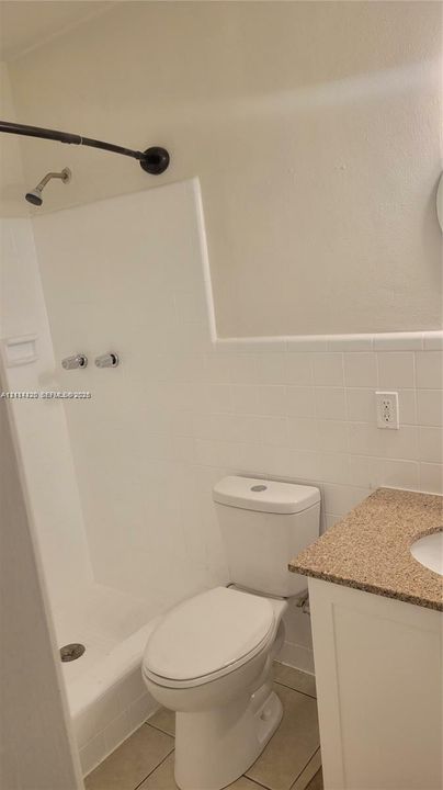 Bathroom featuring a shower with a surround, white ceramic wall tile, a vanity with a neutral-toned countertop, and tile flooring