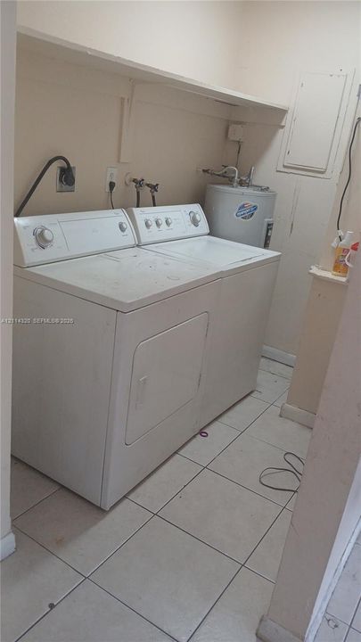 Utility area featuring ceramic tile flooring, an overhead storage shelf, and dedicated water heater enclosure
