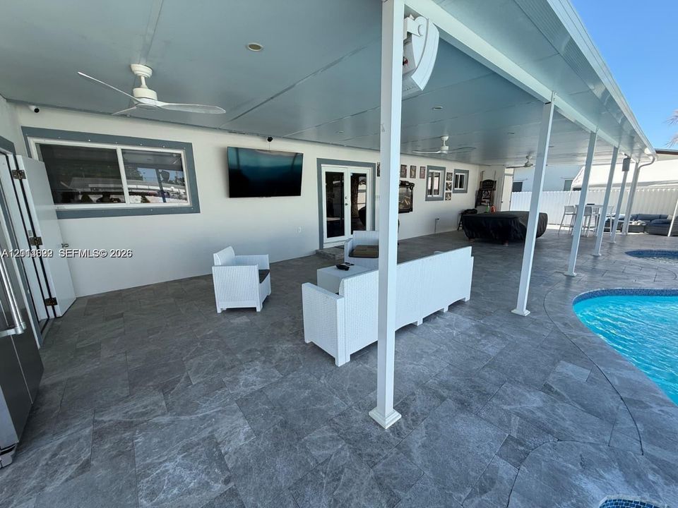 Covered patio featuring stone-tile flooring, ceiling fans, recessed lighting, and a swimming pool