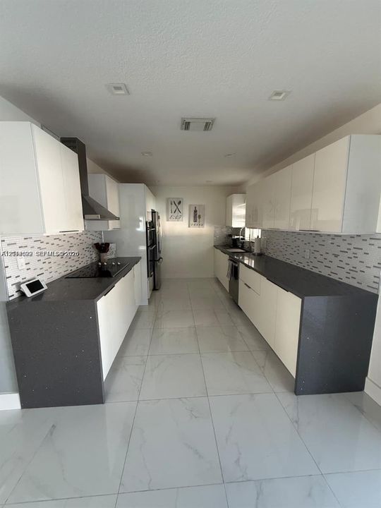 Kitchen featuring sleek white cabinetry, dark countertops, mosaic tile backsplash, recessed lighting, and large-format porcelain tile flooring