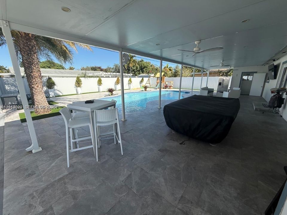 Covered patio featuring large-format tile flooring and ceiling-mounted fans, overlooking a swimming pool enclosed by privacy fencing