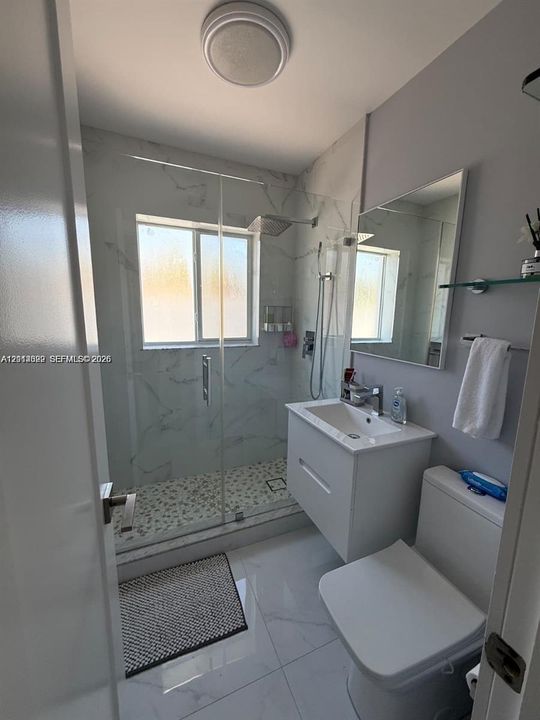 Bathroom featuring a floating vanity with a rectangular sink, walk-in shower with stone-patterned wall tile, pebble-style shower floor, and large-format porcelain floor tiling