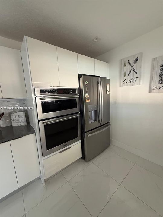 Kitchen featuring flat-panel white cabinetry, stainless steel double wall oven, matching French-door refrigerator, and large-format tile flooring