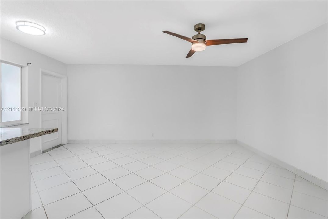 Neutral interior featuring large-format diagonal tile flooring, a modern three-blade ceiling fan with integrated lighting, a flush-mount circular ceiling fixture, and a granite-topped peninsula