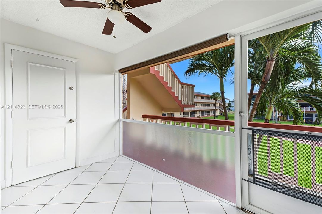 Enclosed balcony featuring white tile flooring, ceiling fan, and privacy screening