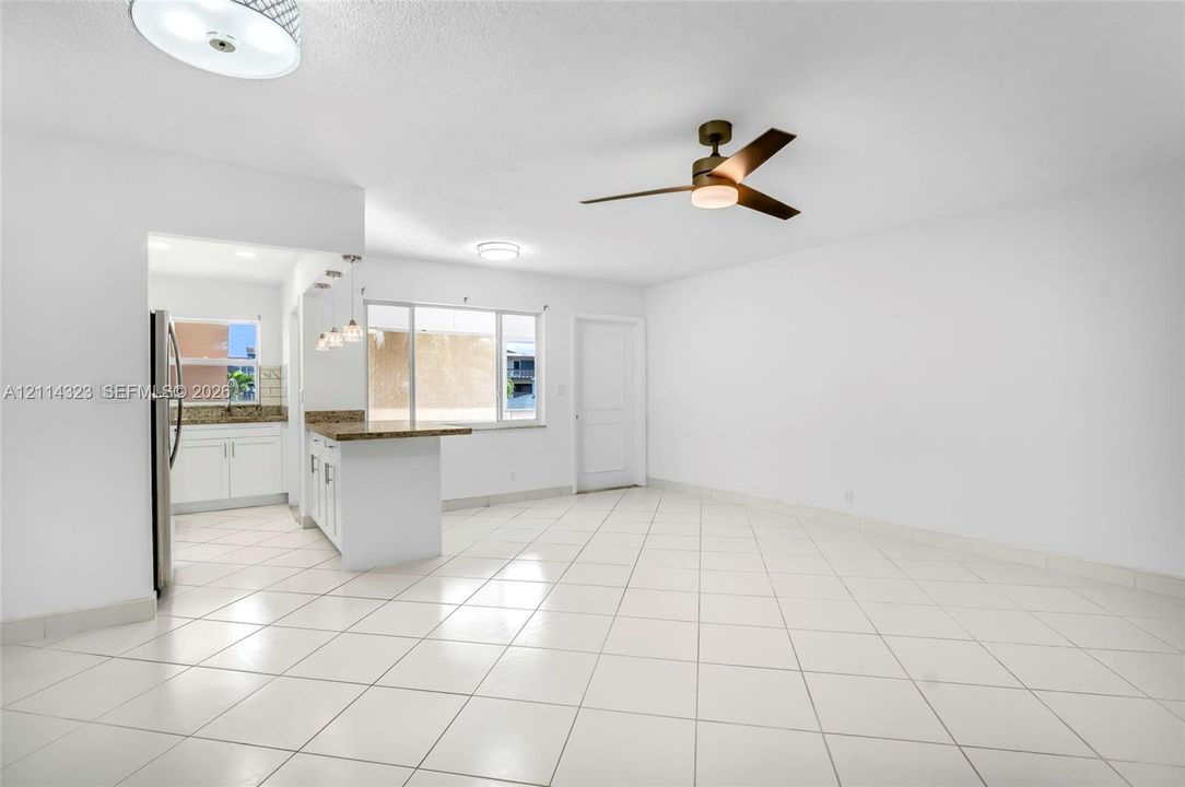 Open floor plan featuring white tile flooring, a kitchen peninsula with stone-finish countertops, three pendant lights, and a ceiling fan with integrated lighting
