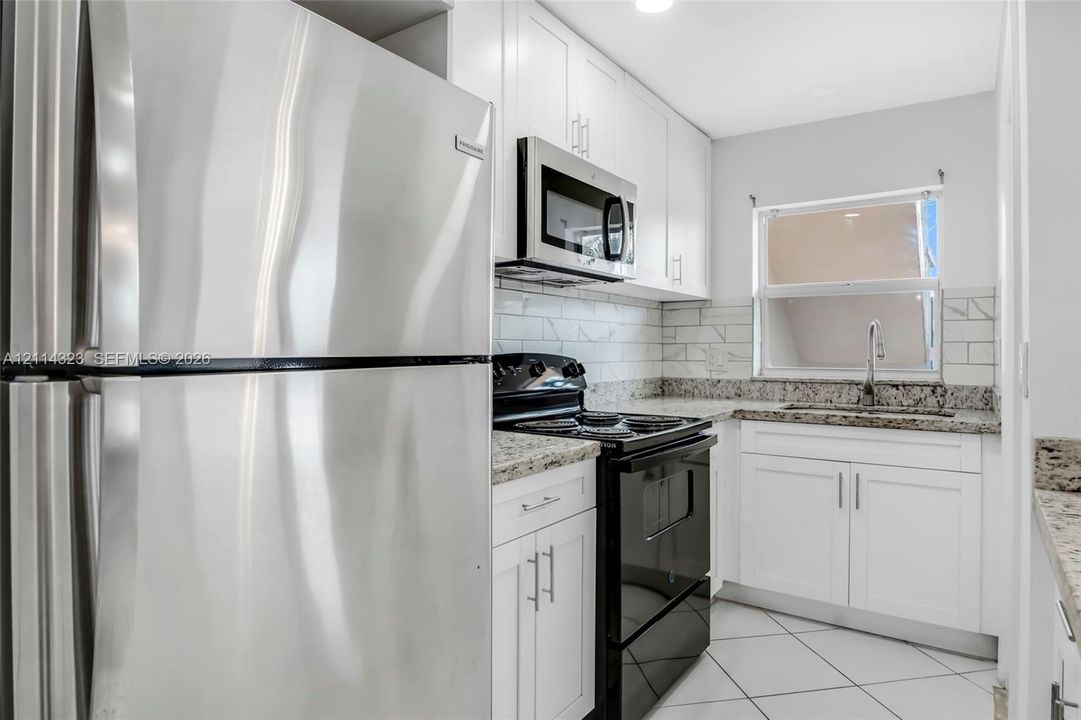 Kitchen featuring white shaker-style cabinetry, stone-finish countertops, subway tile backsplash, stainless steel refrigerator, and built-in microwave