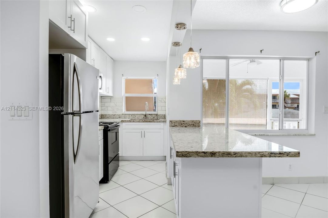Kitchen featuring white shaker-style cabinetry, stone-finish countertops, tile flooring, subway tile backsplash, and decorative pendant lighting