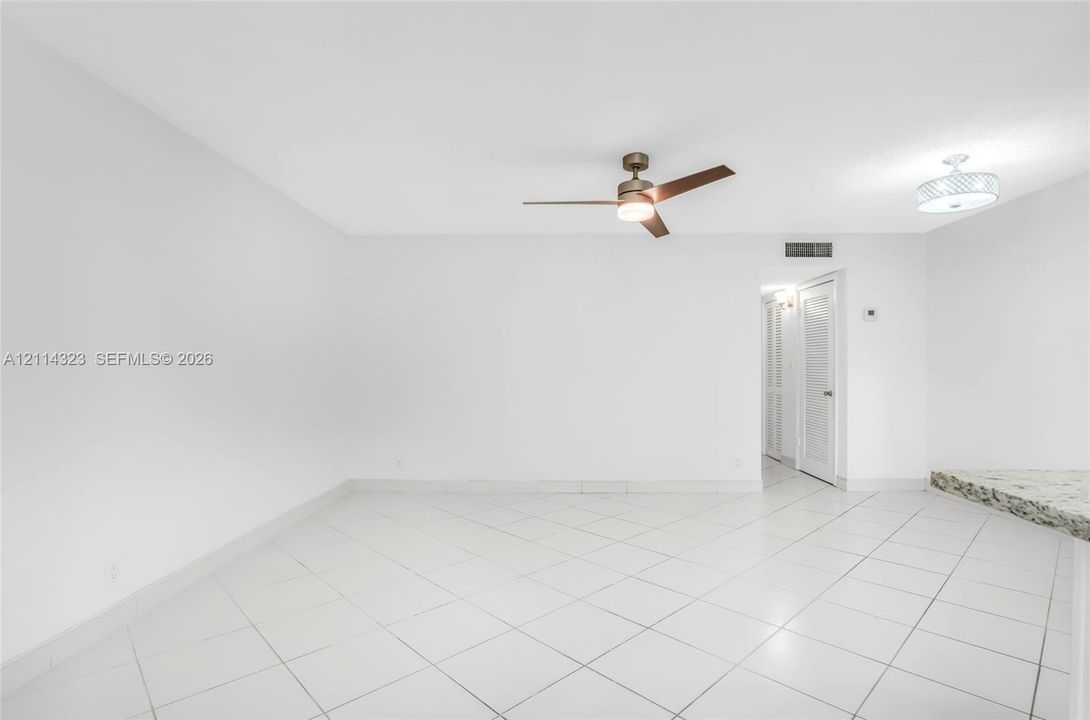 Neutral-toned tile flooring, multi-blade ceiling fan with integrated lighting, overhead circular flush-mount fixture, and stone-finish countertop surface