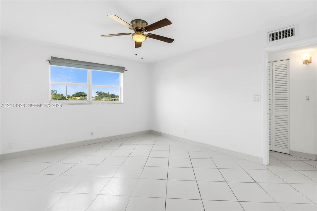 Interior room featuring neutral ceramic tile flooring, a multi-blade ceiling fan with integrated lighting, and louvered closet doors