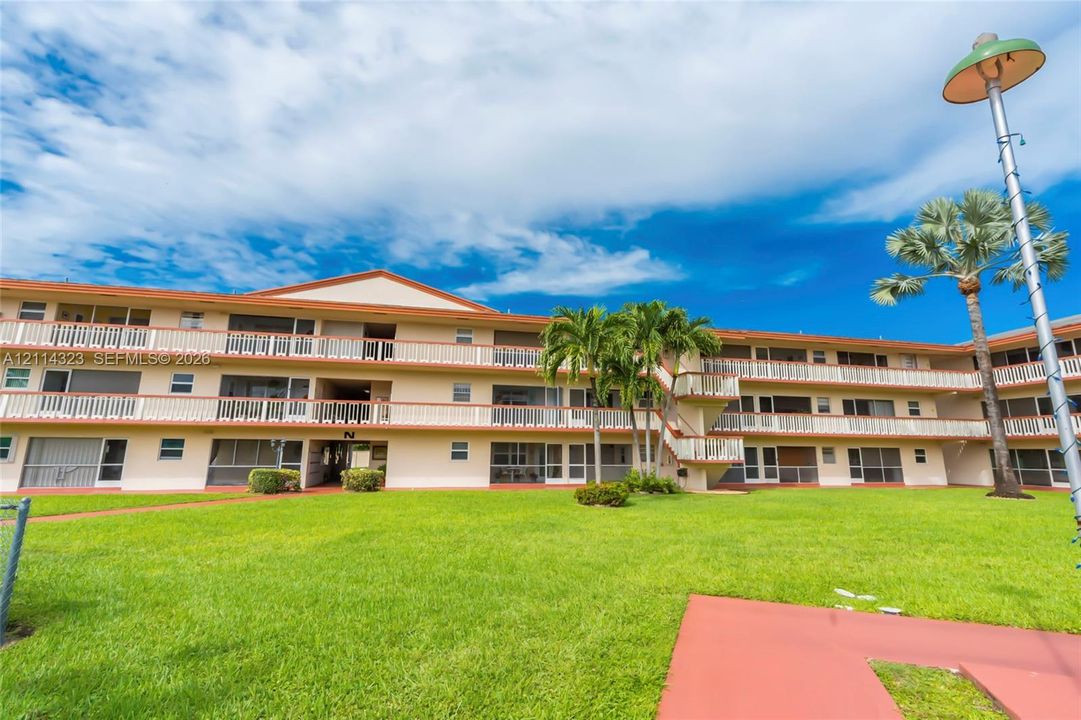 Three-story residential exterior featuring white balconies, a mansard roofline, and manicured green space