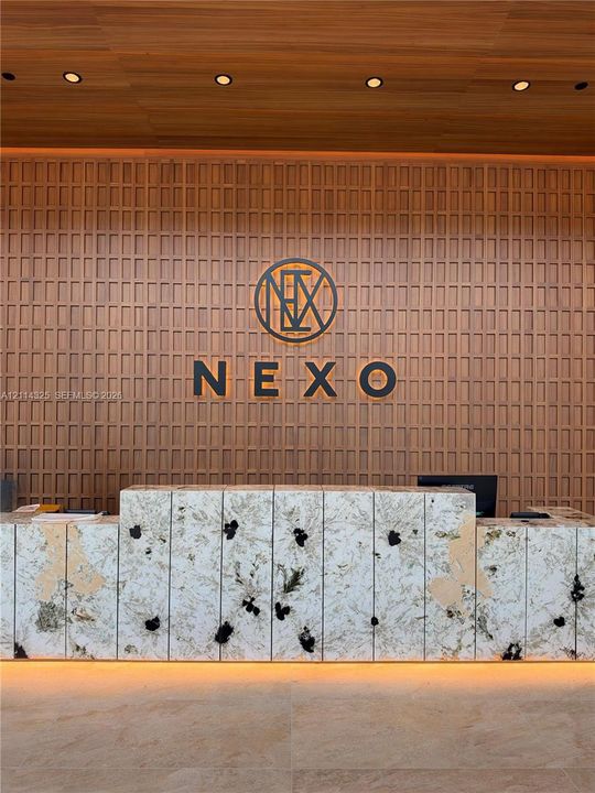 Reception desk featuring a stone facade with integrated base lighting, set against a floor-to-ceiling wood-panel accent wall with recessed ceiling lighting