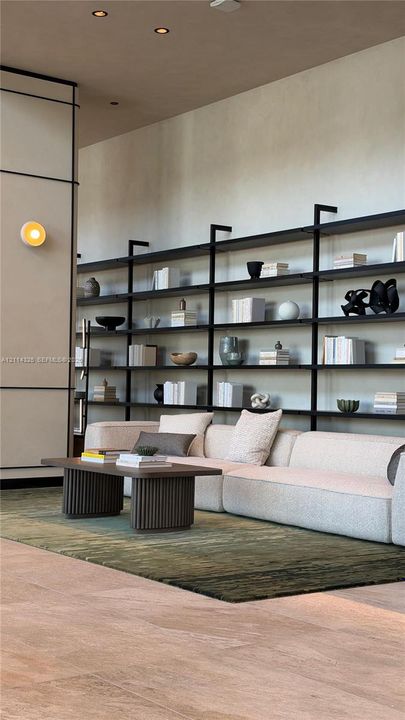 Floor-to-ceiling custom matte black metal shelving, recessed ceiling lighting, wall-mounted circular sconce, paneled accent wall, and stone-finish flooring