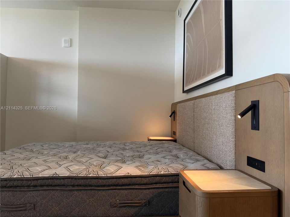 Custom-integrated wood headboard with recessed fabric paneling, matching integrated nightstands, and wall-mounted adjustable reading lights
