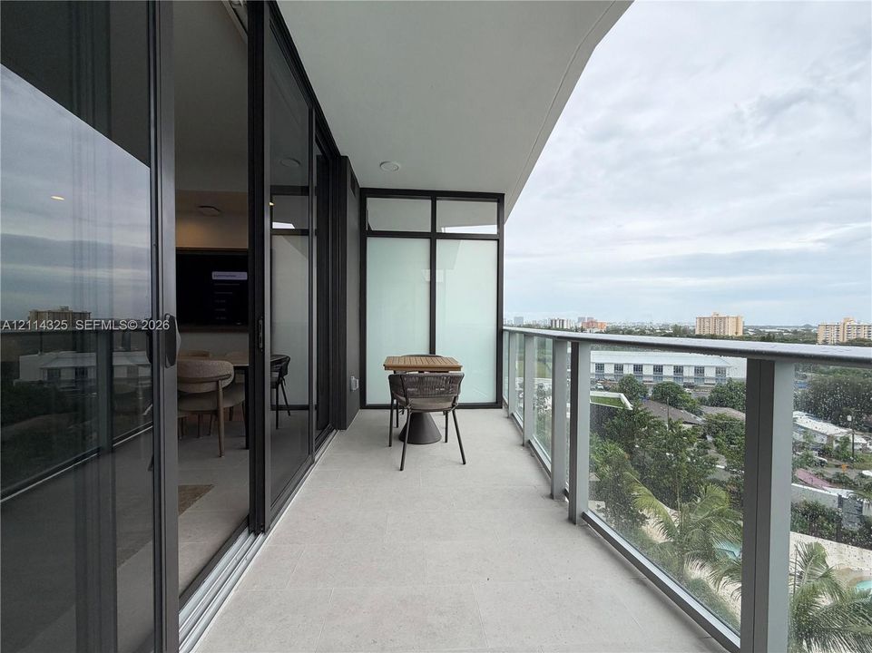 Covered balcony featuring expansive sliding glass doors, a glass paneled railing, and neutral flooring