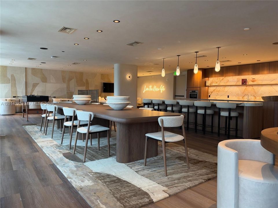 Open-concept area featuring wood-finish flooring, a long built-in bar with stone-surfaced countertops, custom recessed lighting, and a prominent wood-paneled island