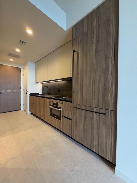 Kitchen featuring wood-finish cabinetry, integrated panel-ready appliances, stone-surface countertops, recessed under-cabinet lighting, and matte black hardware