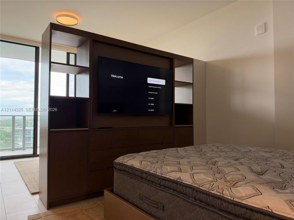 Built-in dark wood storage cabinetry featuring open shelving and integrated drawer units, floor-to-ceiling glass paneling, and flush-mount circular overhead lighting