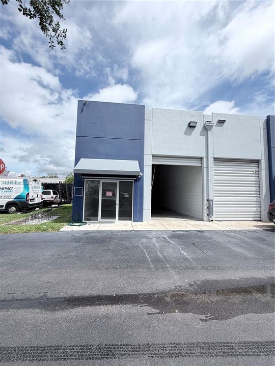 Commercial facade featuring a concrete tilt-up exterior, aluminum-framed glass storefront, metal overhead roll-up door, and architectural metal awning