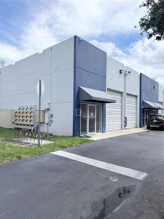 Commercial exterior featuring concrete tilt-wall construction, metal roll-up doors, and aluminum entrance awnings