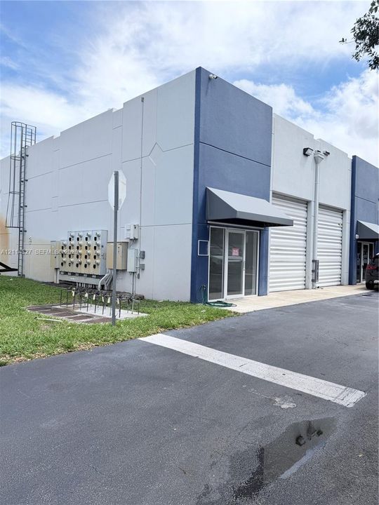 Concrete tilt-wall construction featuring two overhead roll-up doors, metal-frame glass entryways, and exterior-mounted security lighting