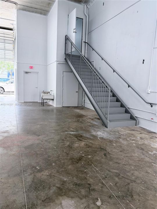 Industrial space featuring high ceilings, concrete flooring, steel staircase with metal railing, and wall-mounted utility sink