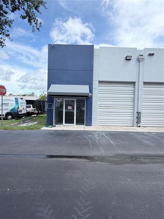 Commercial exterior featuring a blue-accented facade, glass-entry door with an overhead awning, and dual roll-up overhead doors