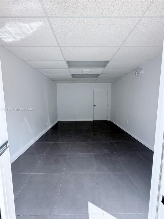 Interior room featuring large-format dark grey tile flooring, neutral wall finishes, and a drop ceiling with recessed lighting