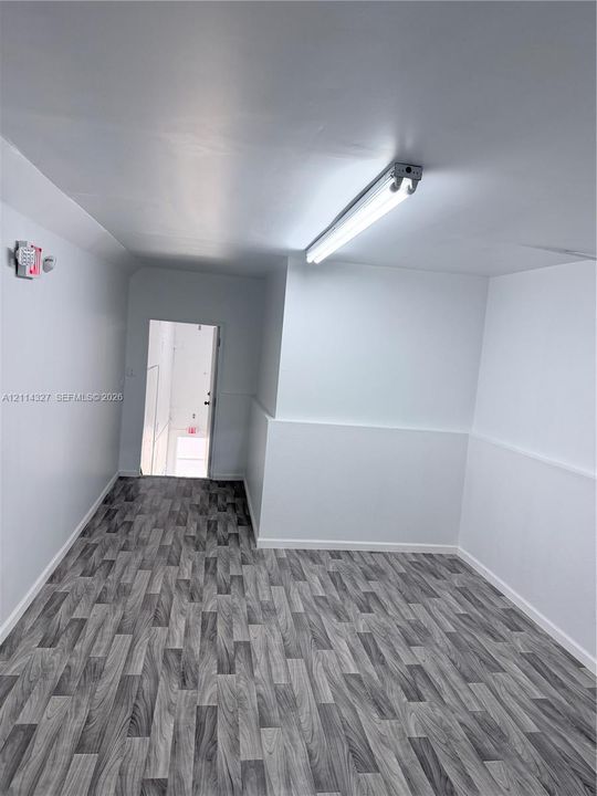 Interior space featuring wood-finish flooring, white wall paneling, and ceiling-mounted linear fluorescent lighting