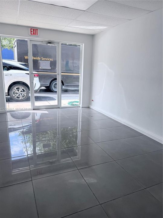Neutral-toned interior featuring large-format polished tile flooring, full-height glass storefront door with side panels, and drop ceiling