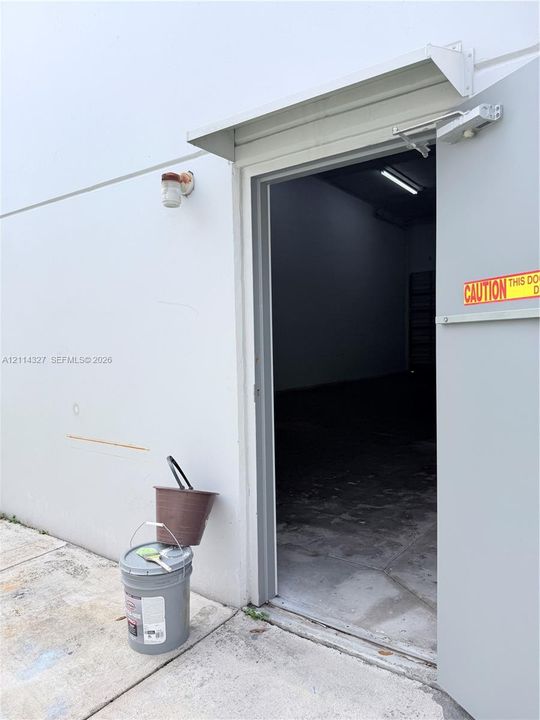 Exterior entry featuring a steel door, overhead metal awning, and wall-mounted exterior light fixture