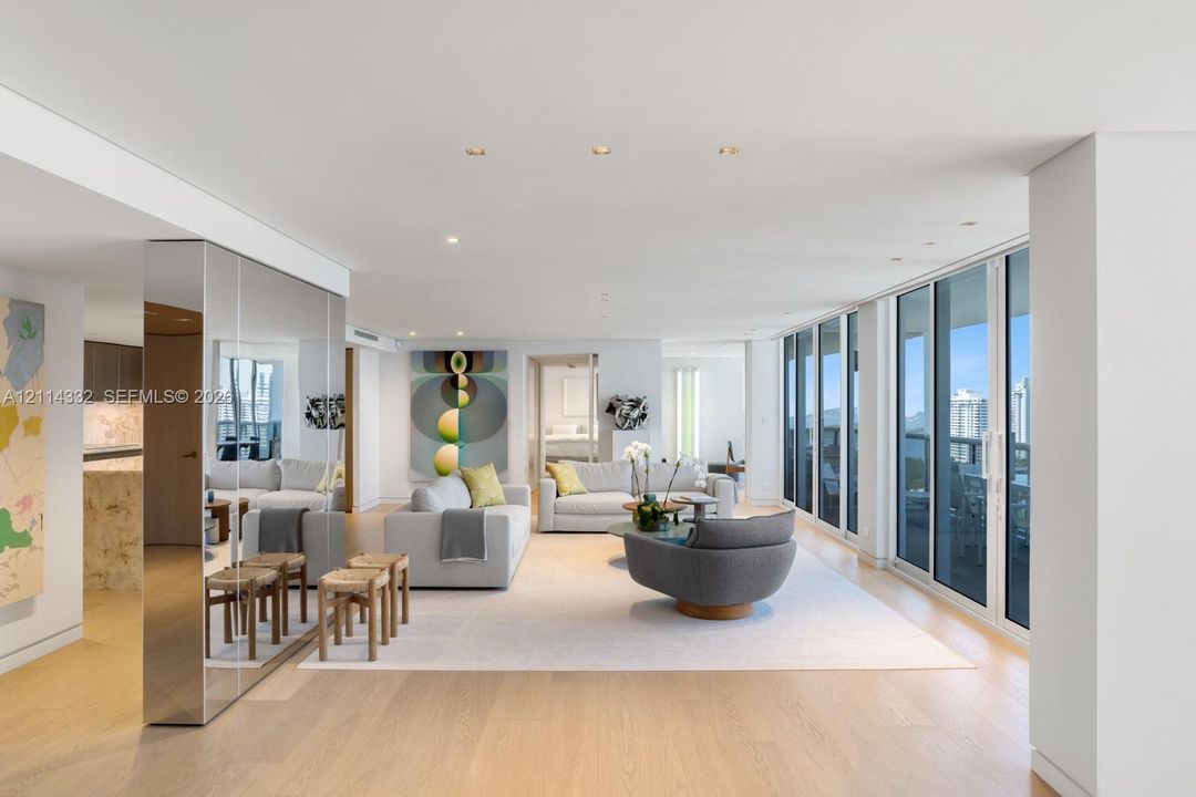 Open-concept living space featuring wood-finish flooring, floor-to-ceiling glass sliding doors, recessed ceiling lighting, and reflective floor-to-ceiling paneling