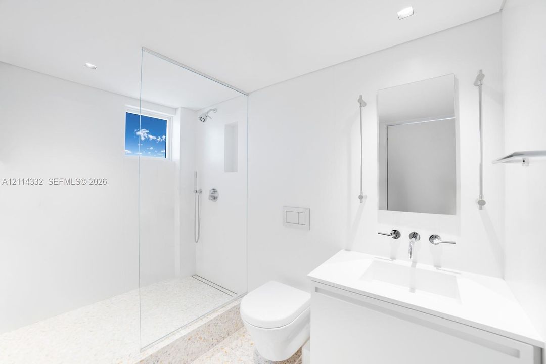 Minimalist bathroom featuring a glass-enclosed shower with a built-in recessed shelf, wall-mounted dual-flush toilet, integrated vanity with a rectangular sink, and polished stone-finish flooring