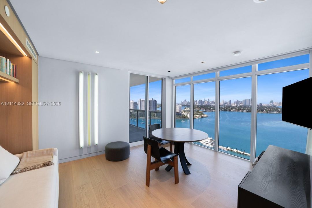 Floor-to-ceiling windows, wood-finish flooring, built-in recessed shelving, integrated lighting, and water-fronting balcony