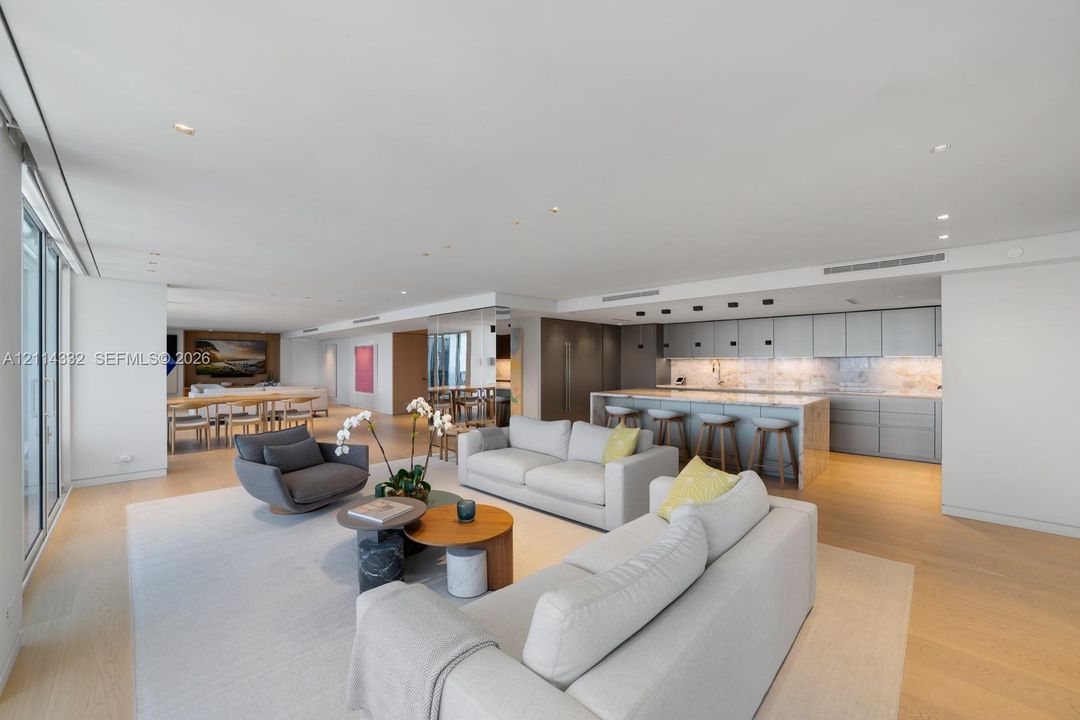 Open-concept main living area featuring light wood-finish flooring, recessed lighting, floor-to-ceiling glass sliding doors, and a chef-inspired kitchen with stone-surfaced island and integrated cabinetry