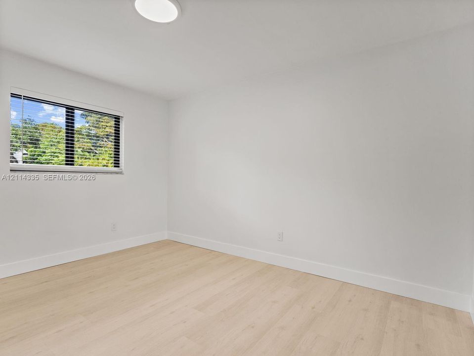Light-filled room featuring wood-finish flooring, a flush-mount circular ceiling light, and a single-pane horizontal window with integrated blinds