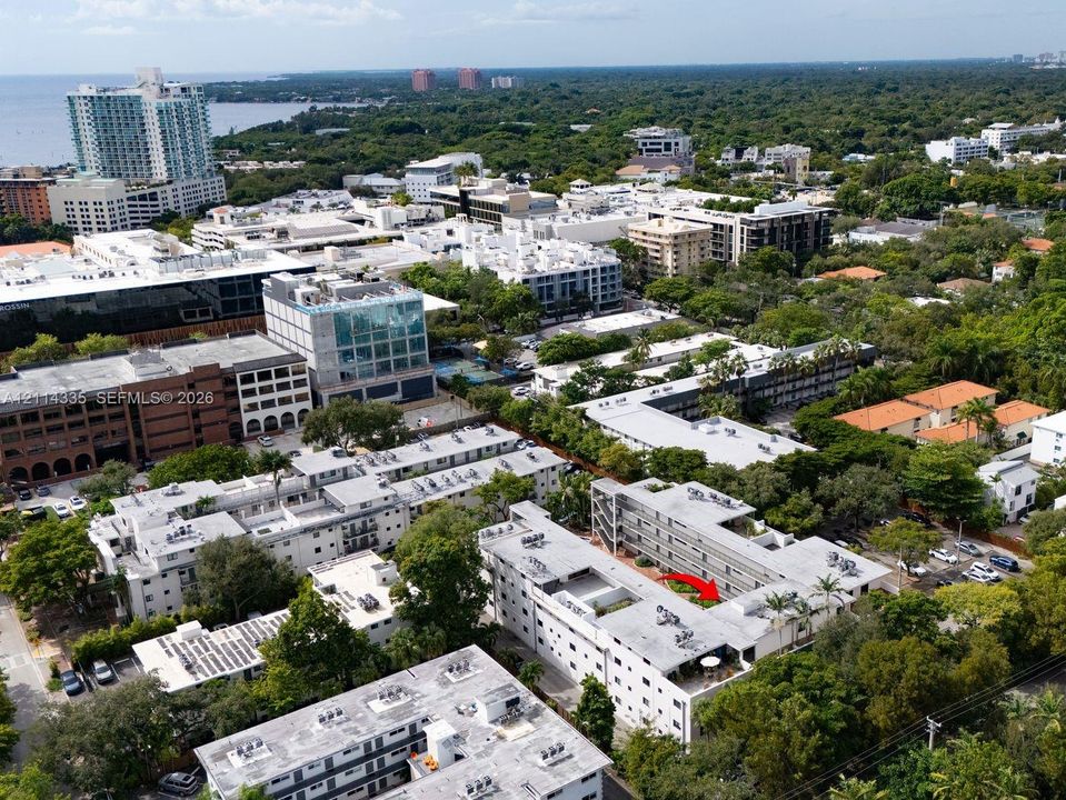 Aerial perspective featuring a multi-story building within a dense urban landscape, exterior paved parking areas, and mature tree canopy