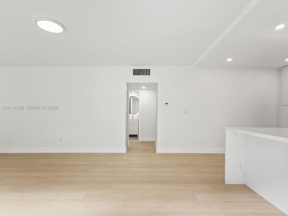 Neutral-toned interior space featuring light wood-finish flooring, recessed ceiling lighting, and a stone-surface waterfall edge island with integrated cabinetry