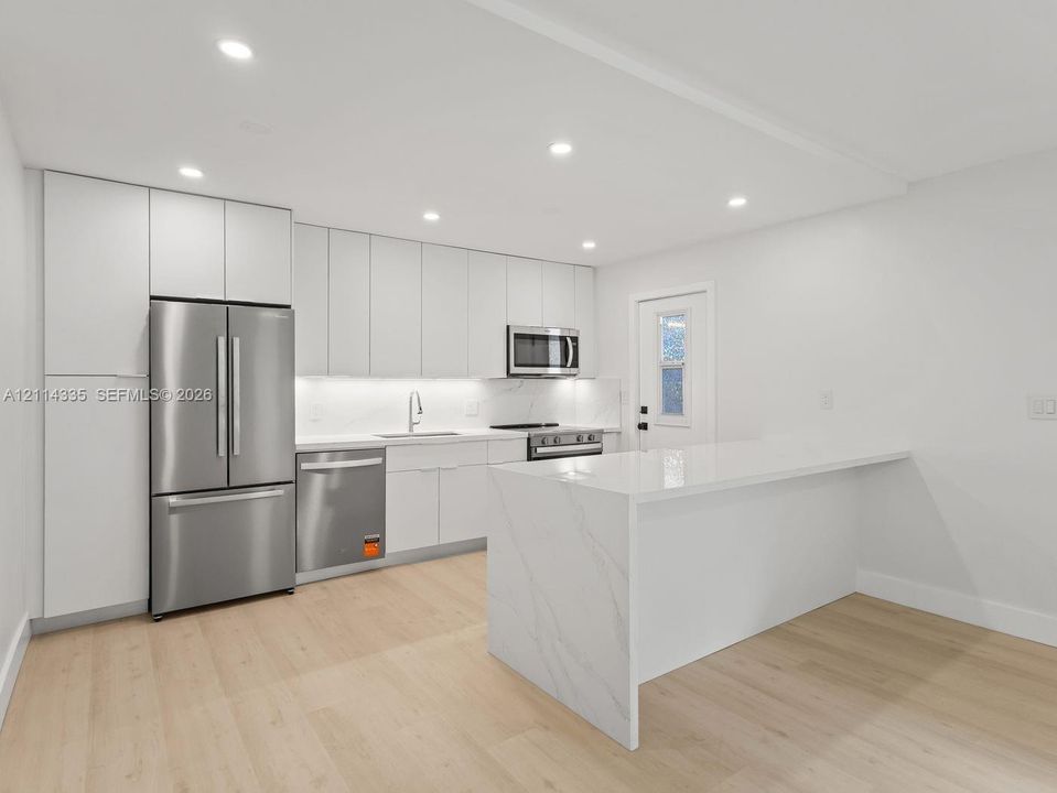 Modern kitchen featuring floor-to-ceiling cabinetry, a waterfall-edge island, integrated stainless steel appliances, recessed lighting, and wood-finish flooring